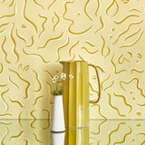 Two vases stand in front of a wall papered in a painterly floral print in yellow and white on a light yellow field.