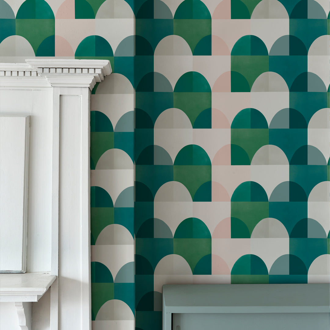 Detail of a room with plaster molding and walls papered in a curvy geometric print in shades of white, pink, blue and green.