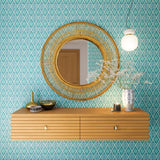 A floating shelf and statement mirror hang on a wall papered in an intricate diamond grid pattern in blue and turquoise.