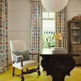 A maximalist study with bright yellow carpet and curtains in a playful rainbow floral print on a white field.