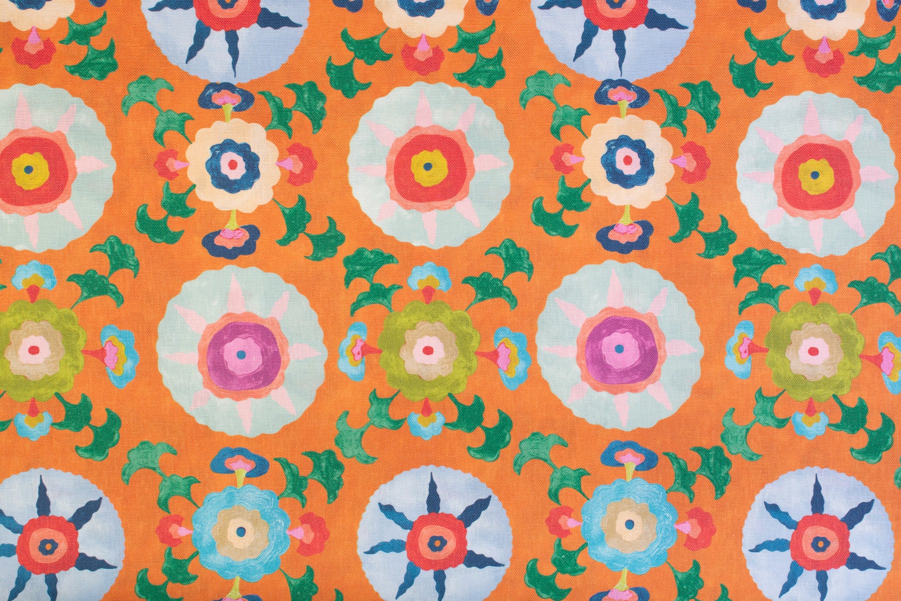 Detail of fabric in a playful floral pattern in a rainbow of colors on an orange field.