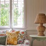 A cozy living room tableau with a couch upholstered in a playful rainbow floral print on a white field.