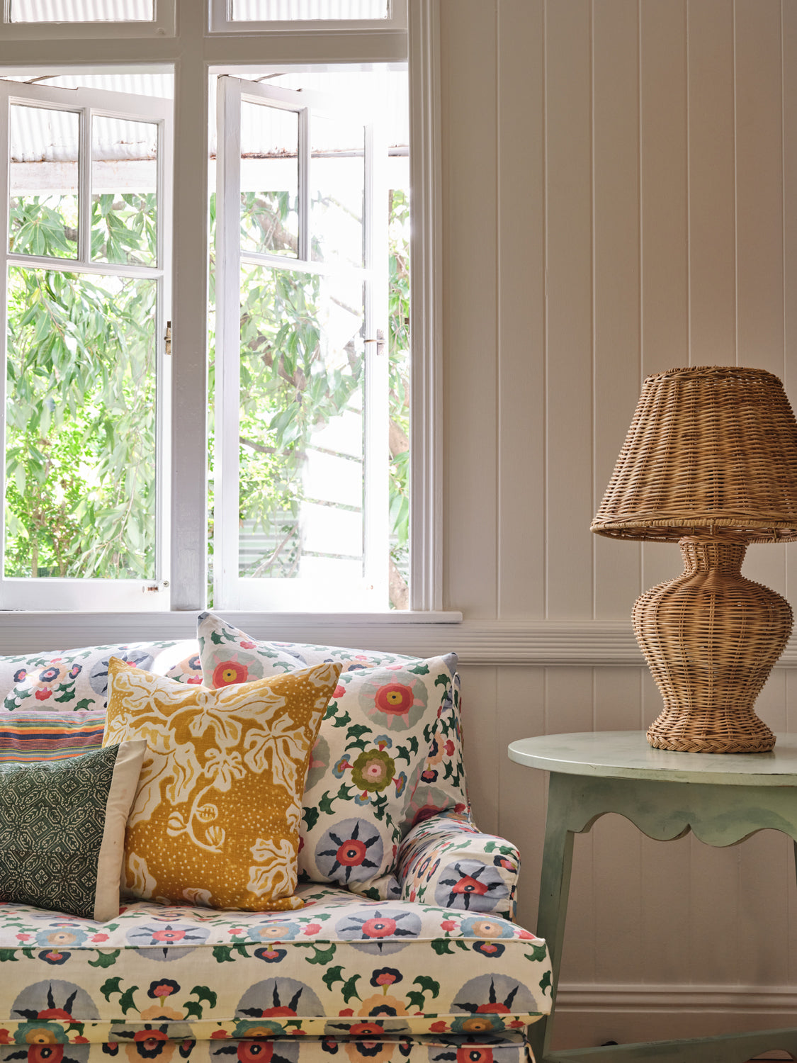 A cozy living room tableau with a couch upholstered in a playful rainbow floral print on a white field.