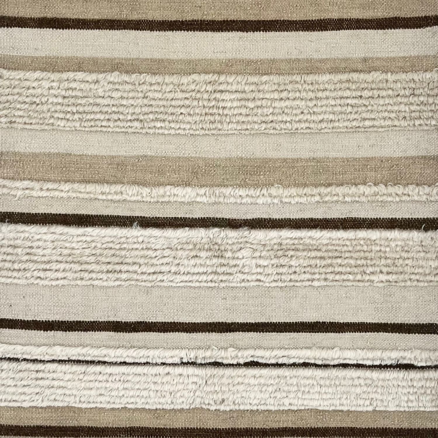 Detail of a flatwoven carpet with tan, beige and brown stripes, with a wide fringed stripe throughout.