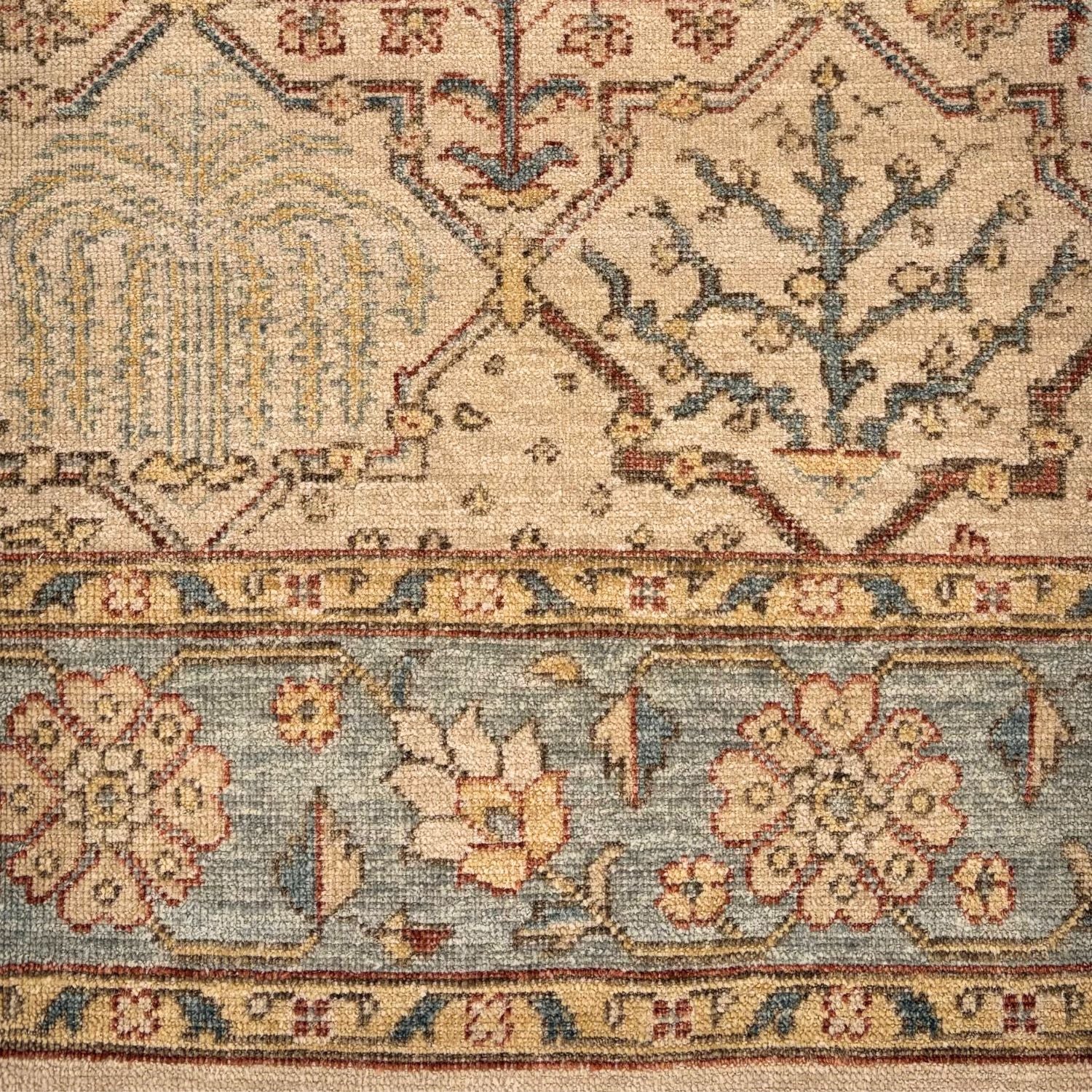Detail of a traditional Old World rug with floral and geometric outlines in shades of tan, rust and blue.