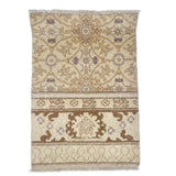 A rug with geometric and floral pattern in taupe, medium brown and lavender.