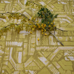 Flowers and branches lie on top of fabric yardage in an abstract geometric pattern in shades of yellow.