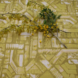 Flowers and branches lie on top of fabric yardage in an abstract geometric pattern in shades of yellow.