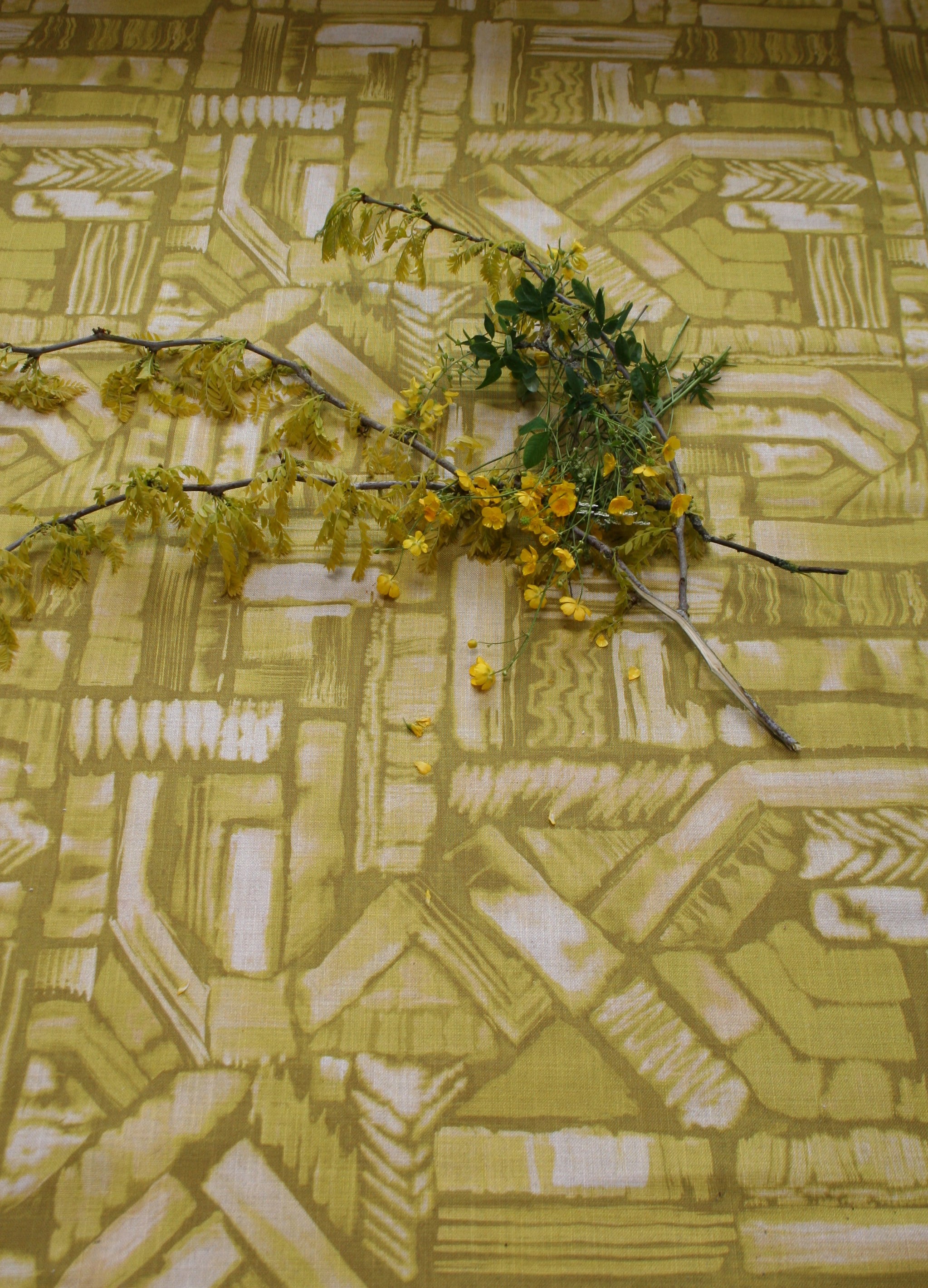 Flowers and branches lie on top of fabric yardage in an abstract geometric pattern in shades of yellow.