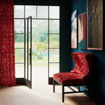 A living space with large windows and an armchair and curtains upholstered in the same abstract geometric print in red.