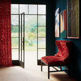 A living space with large windows and an armchair and curtains upholstered in the same abstract geometric print in red.