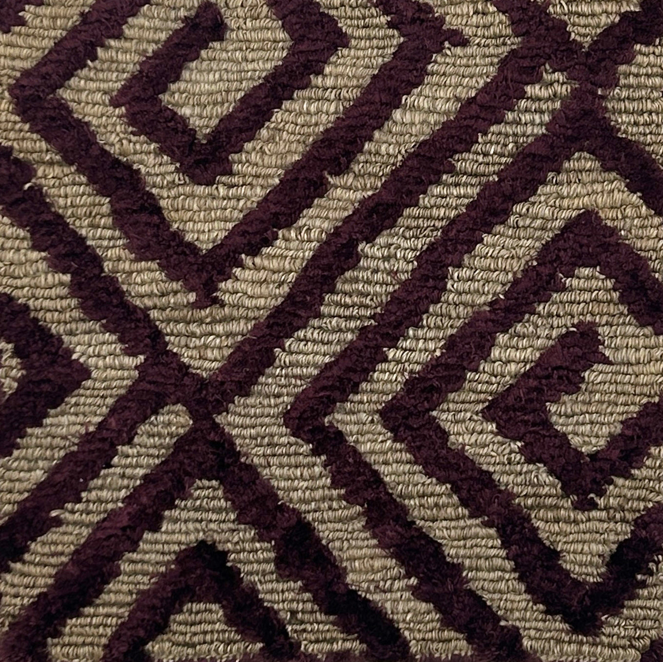 Close-up of a handknotted rug with a purple geometric pattern on a beige background