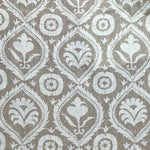 Detail of fabric in a floral damask print in white on a light brown field.