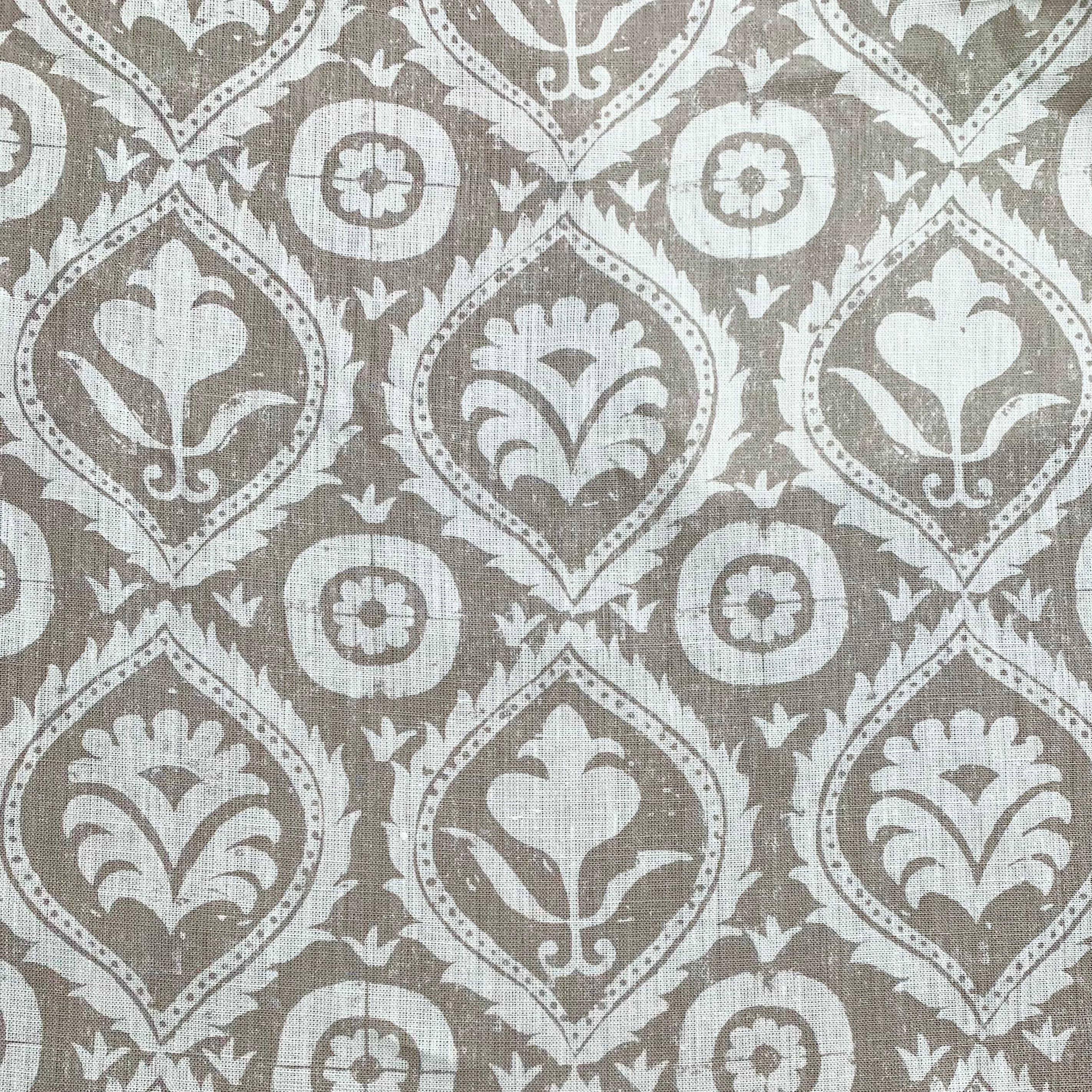 Detail of fabric in a floral damask print in white on a light brown field.