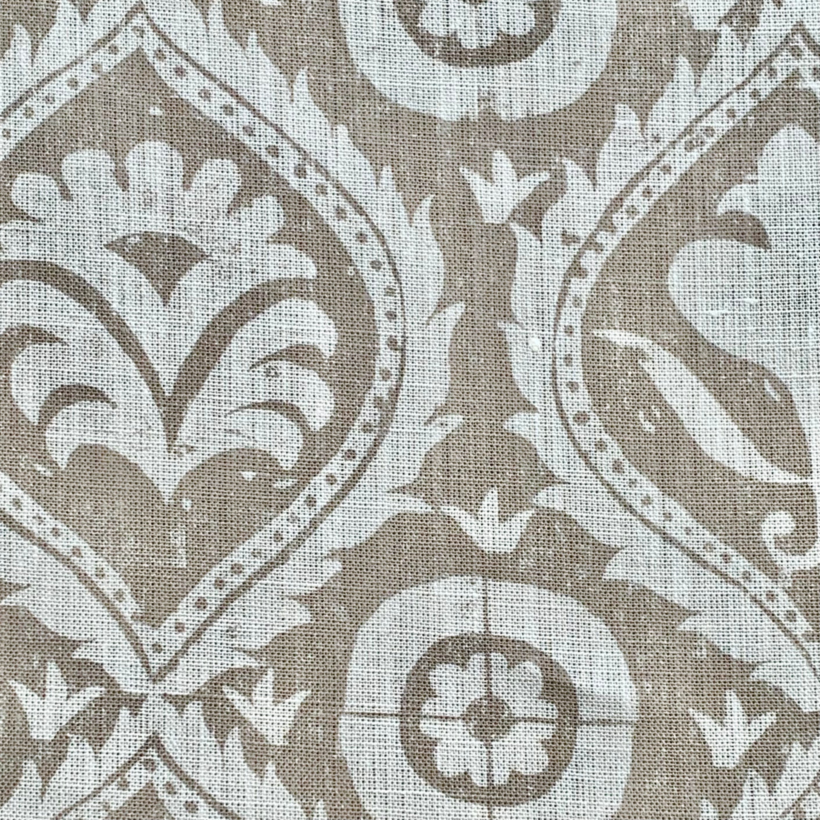 Close-up of fabric in a floral damask print in white on a light brown field.