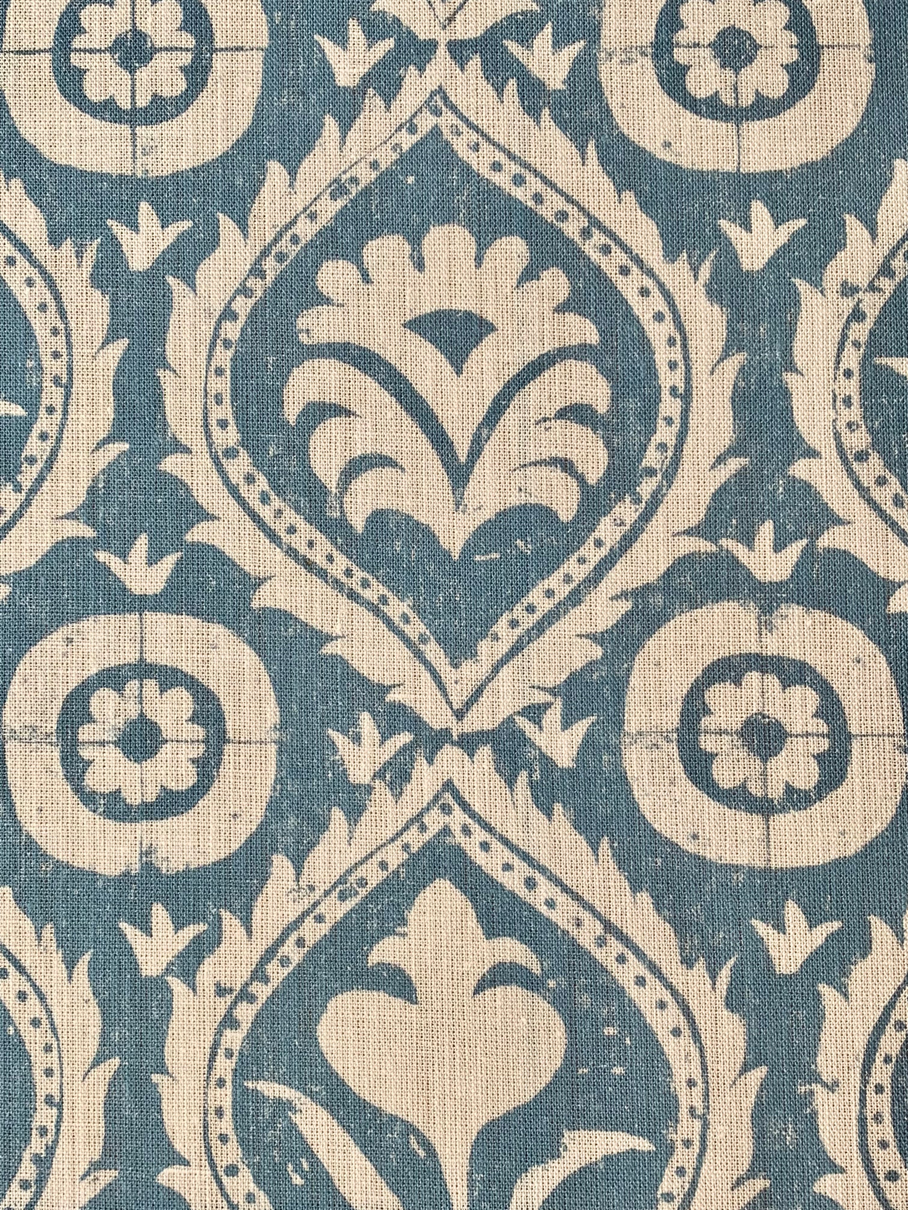 Close-up of fabric in a floral damask print in tan on a blue field.