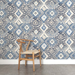 A wooden chair stands in front of a wall papered in a painterly diamond print in shades of blue, tan and gray.