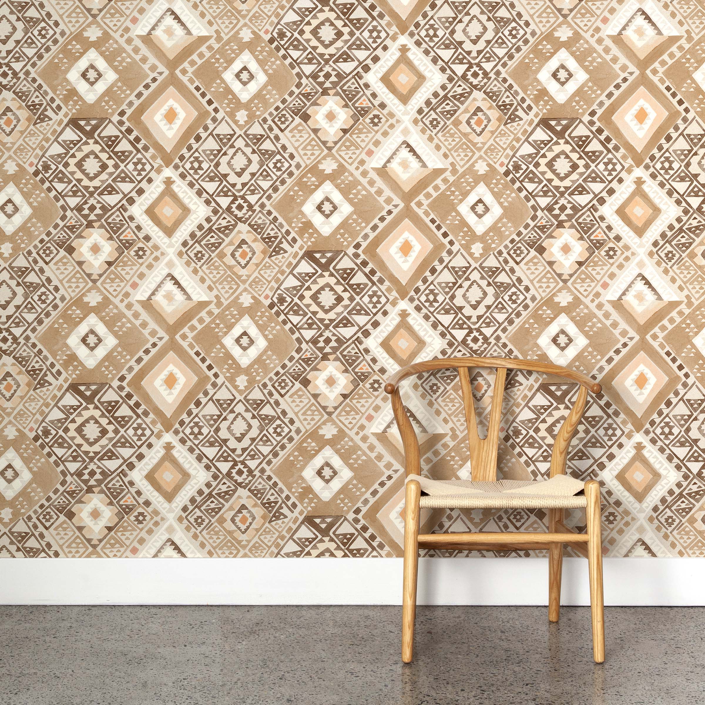 A wooden chair stands in front of a wall papered in a painterly diamond print in shades of brown, tan and white.