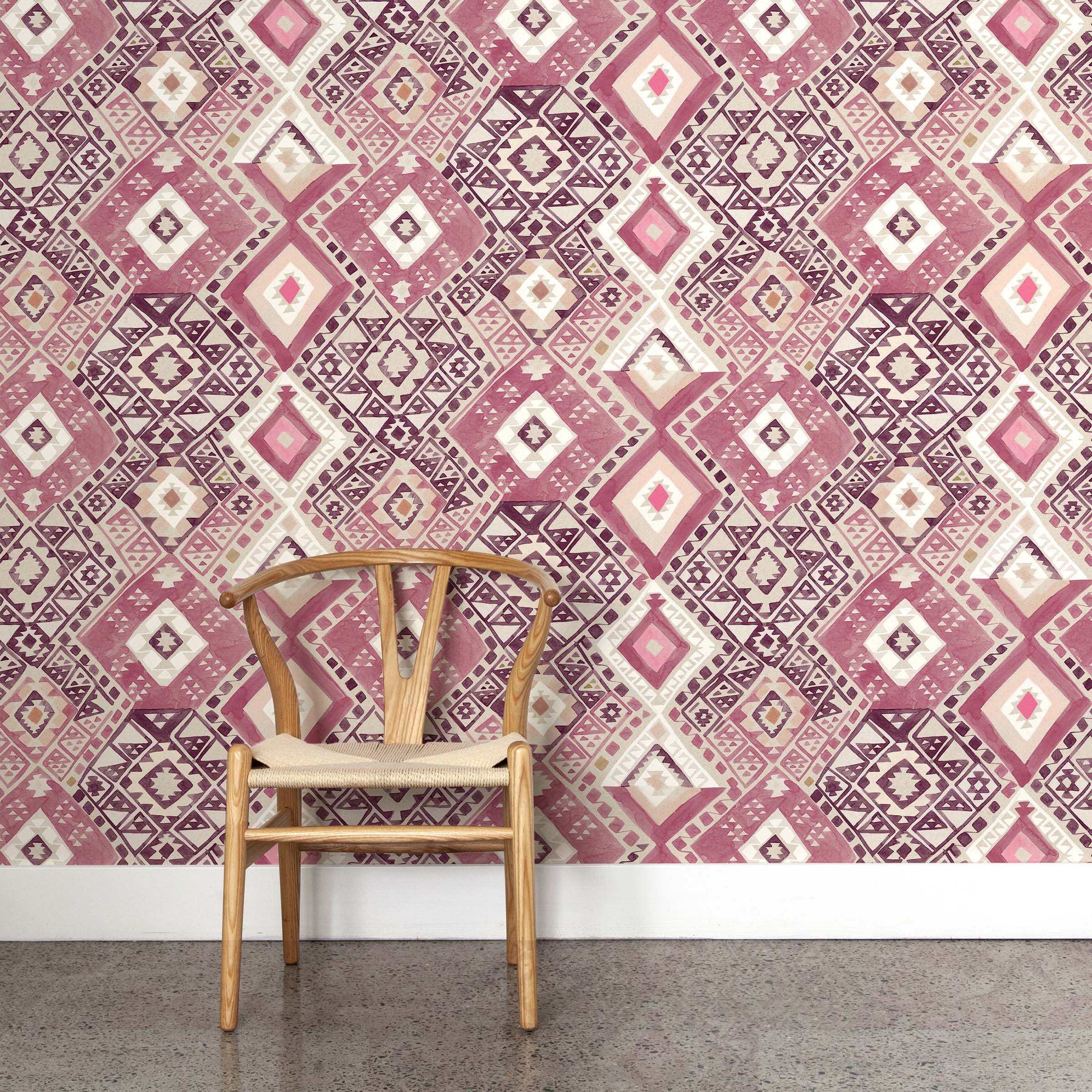 A wooden chair stands in front of a wall papered in a painterly diamond print in shades of pink, tan and white.