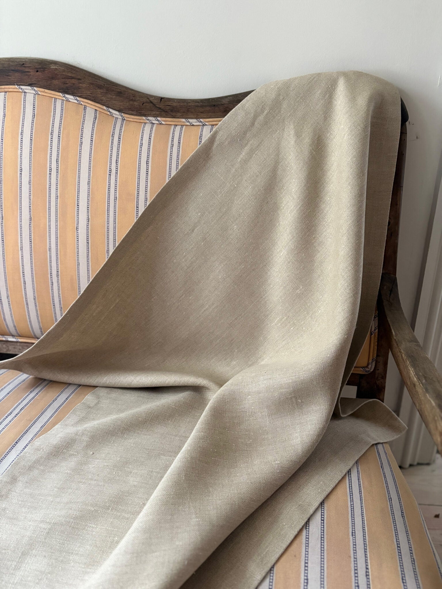 Beige linen draped over a striped chair with a white wall background