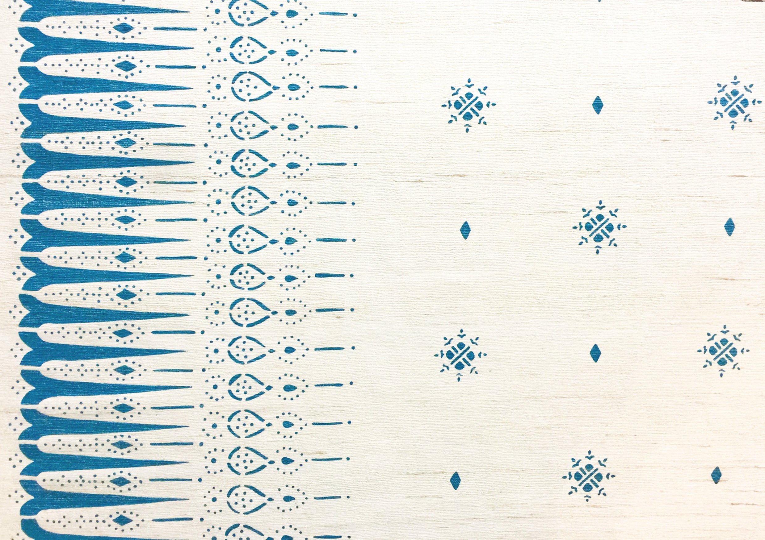 Detail of fabric in a bordered teardrop print in blue on a cream field.