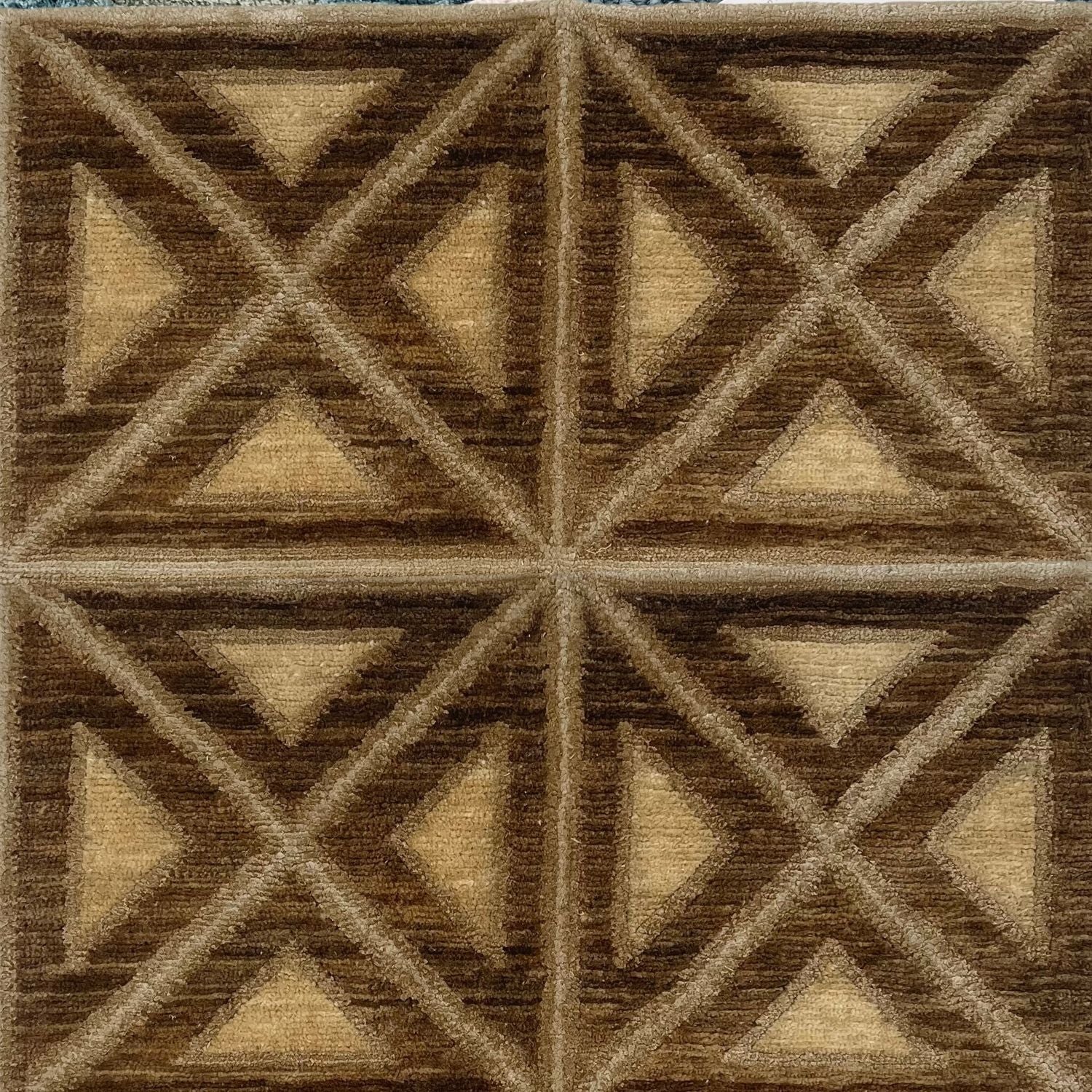 A rug woven in a repeating diamond and square pattern in brown, tan and beige.