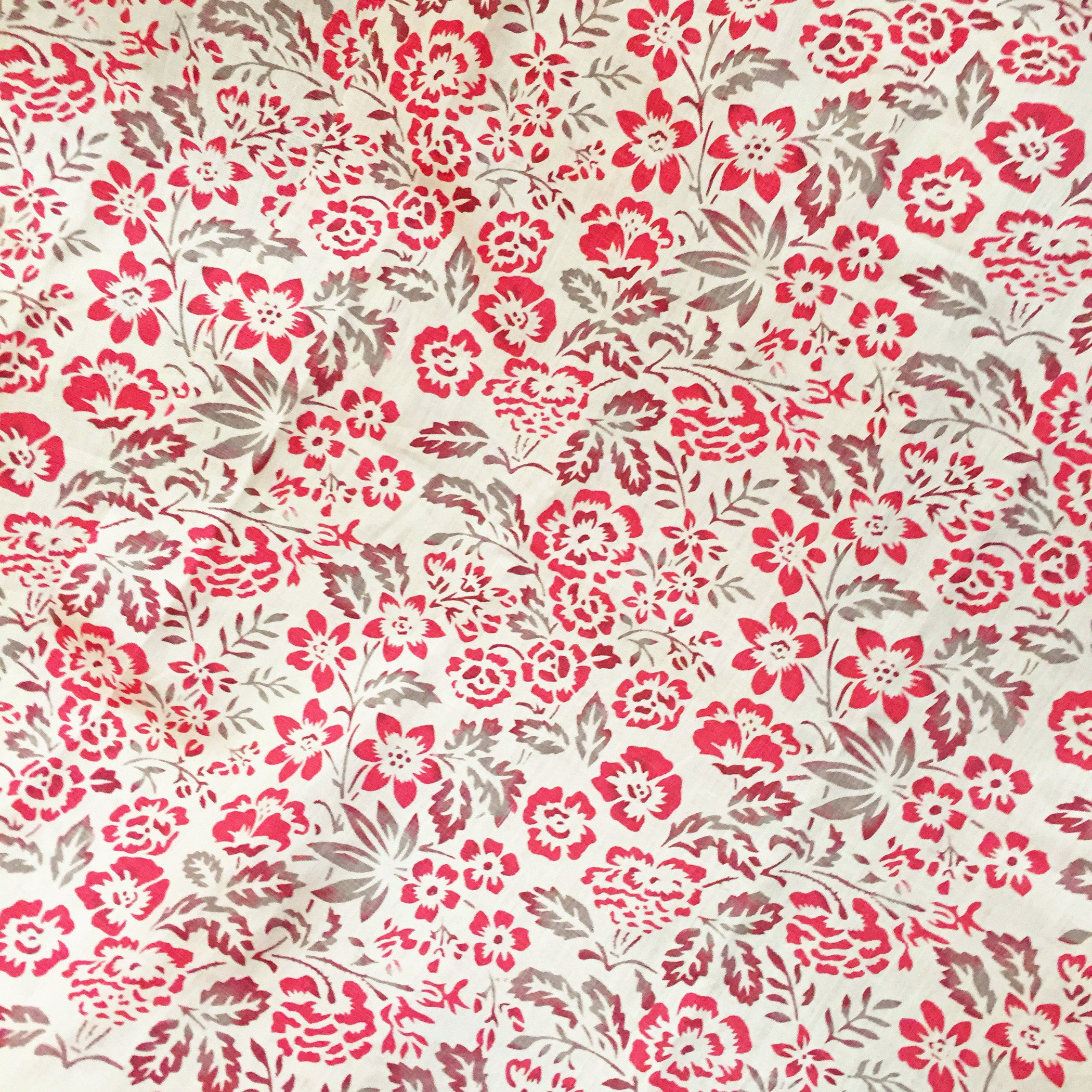 Detail of fabric in a floral print in mottled pink, red and gray on a cream field.