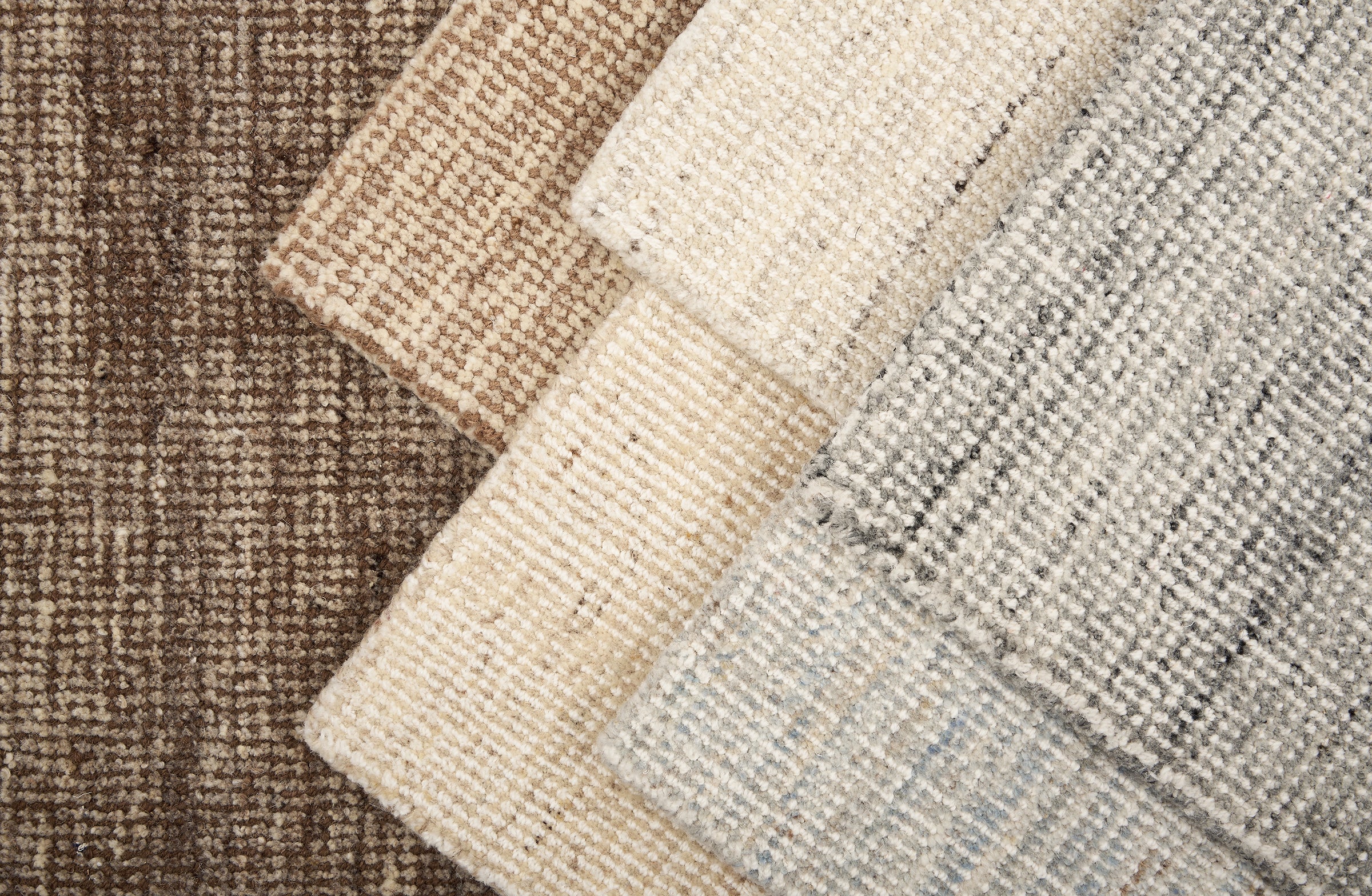 Stack of broadloom carpet samples in a textural design in a range of neutrals randing from ivory, to grey to brown.