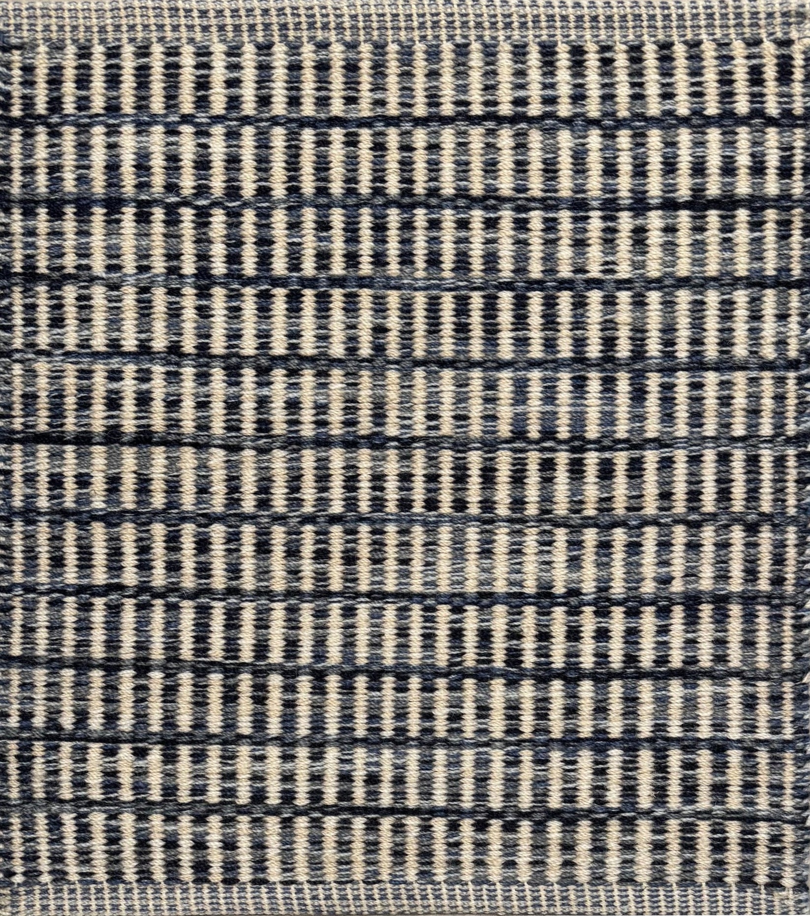 Textured rug with a striated navy blue and cream checker pattern