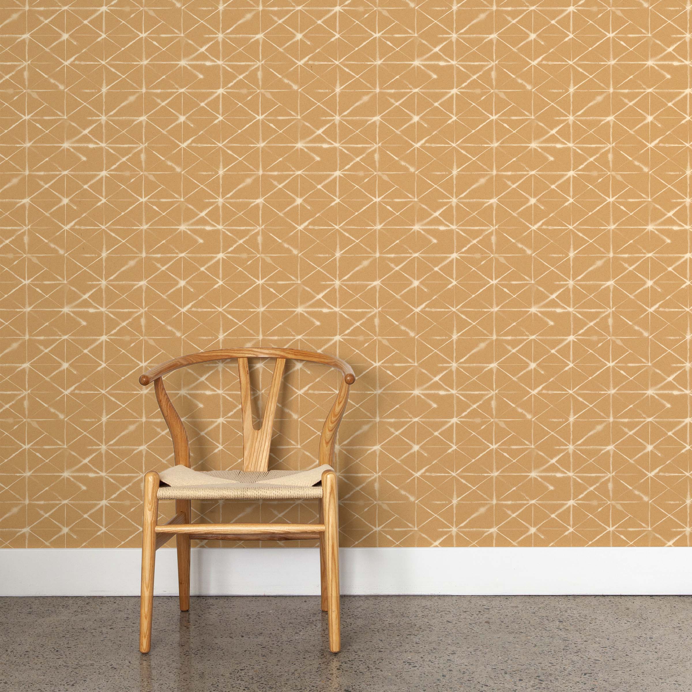 A wooden chair stands in front of a wall papered in a mottled lattice print in white on a burnt orange field.