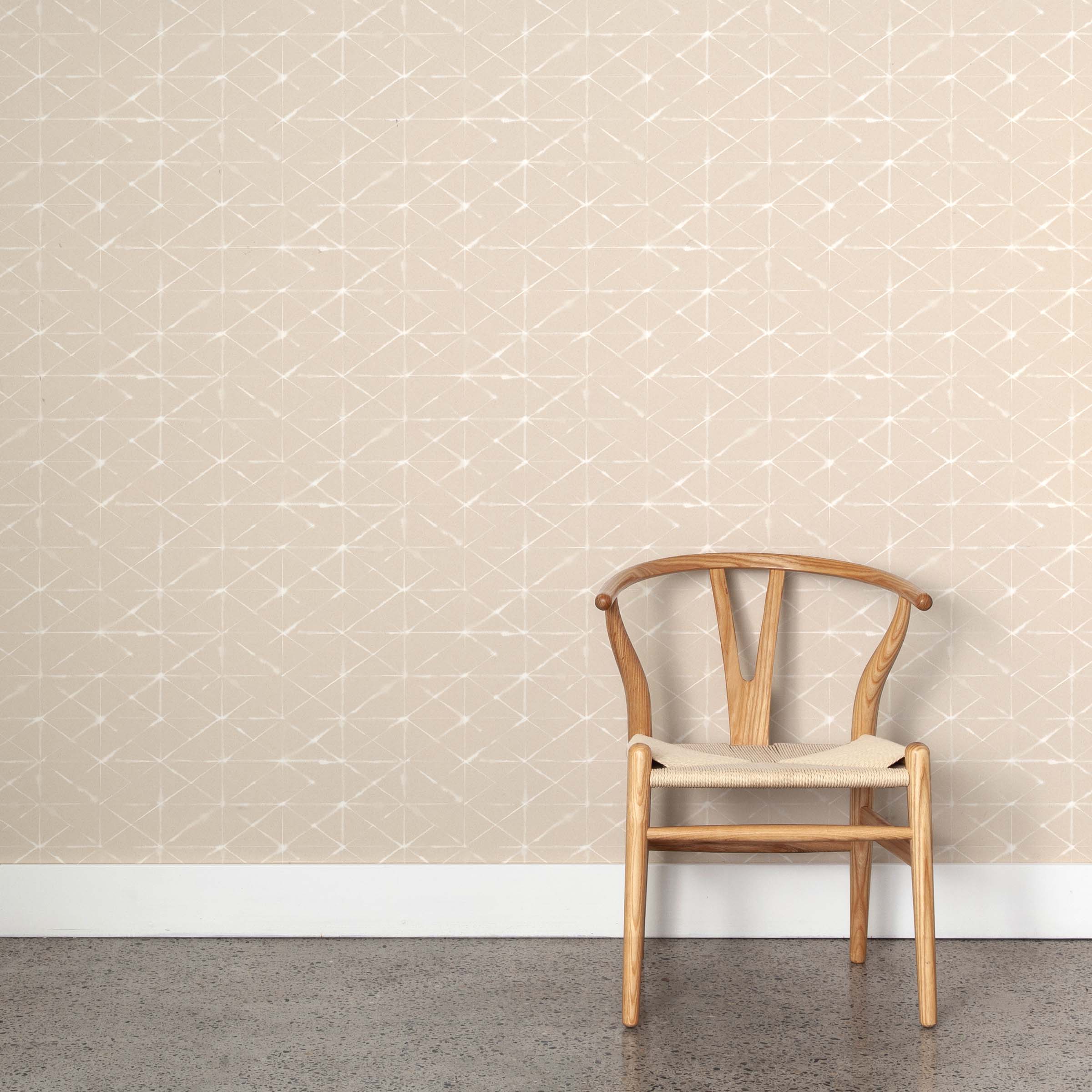 A wooden chair stands in front of a wall papered in a mottled lattice print in white on a cream field.