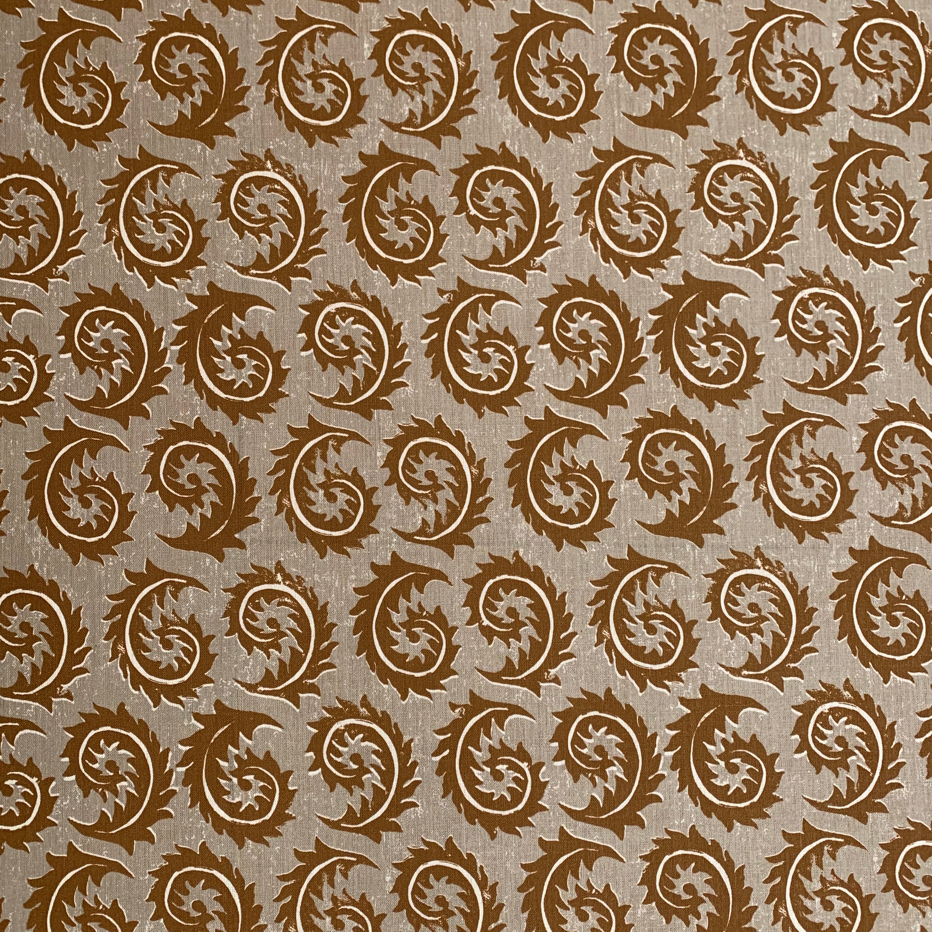 Detail of fabric in a repeating curved leaf print in white and brown on a tan field.