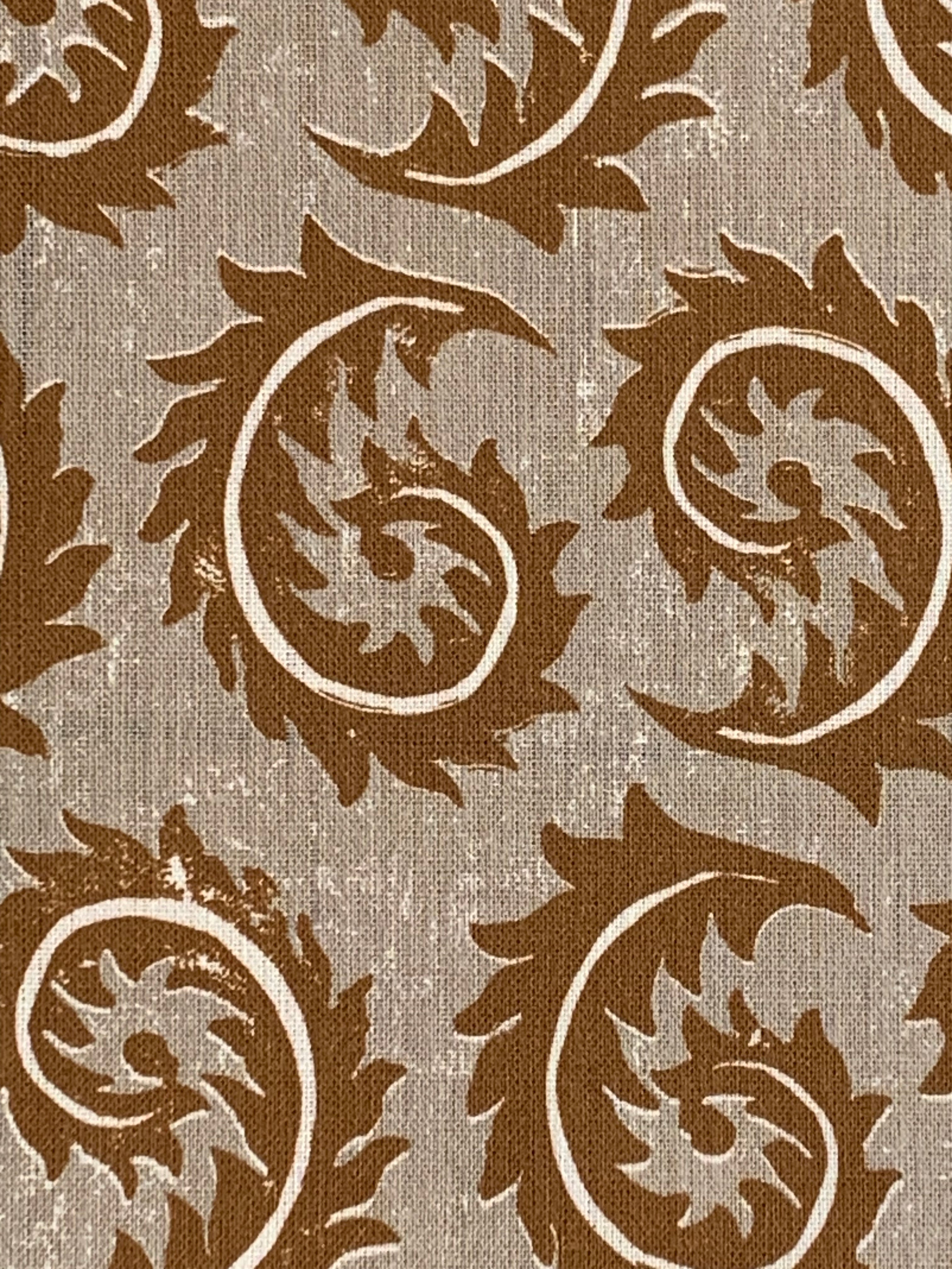 Close-up of fabric in a repeating curved leaf print in white and brown on a tan field.