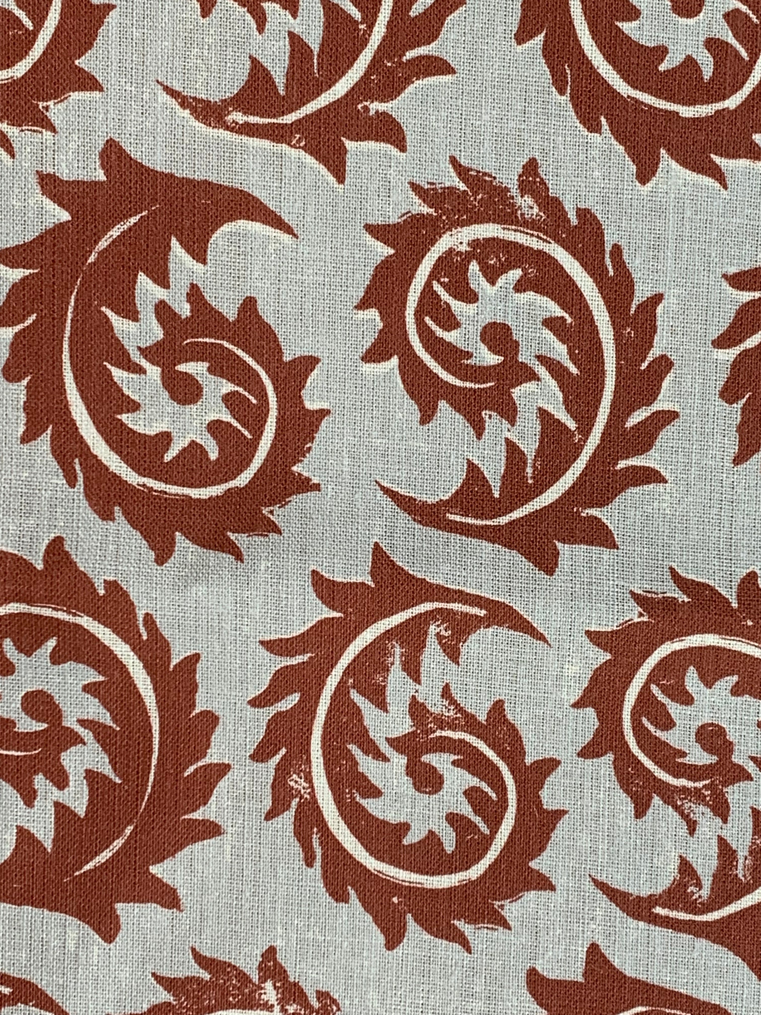 Close-up of fabric in a repeating curved leaf print in white and brown on a gray field.