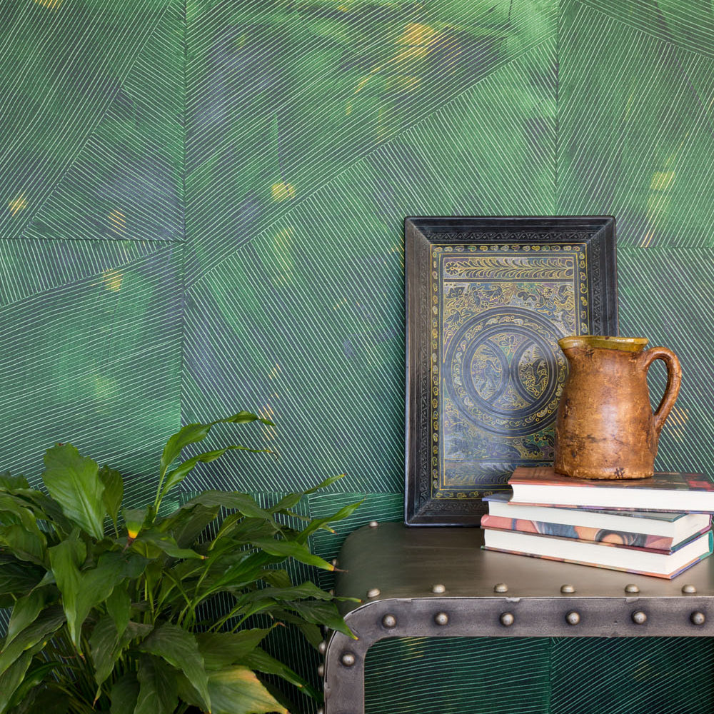 A large plant and an end table stand in front of a wall covered in multi-directional combed wallpaper in mottled green.