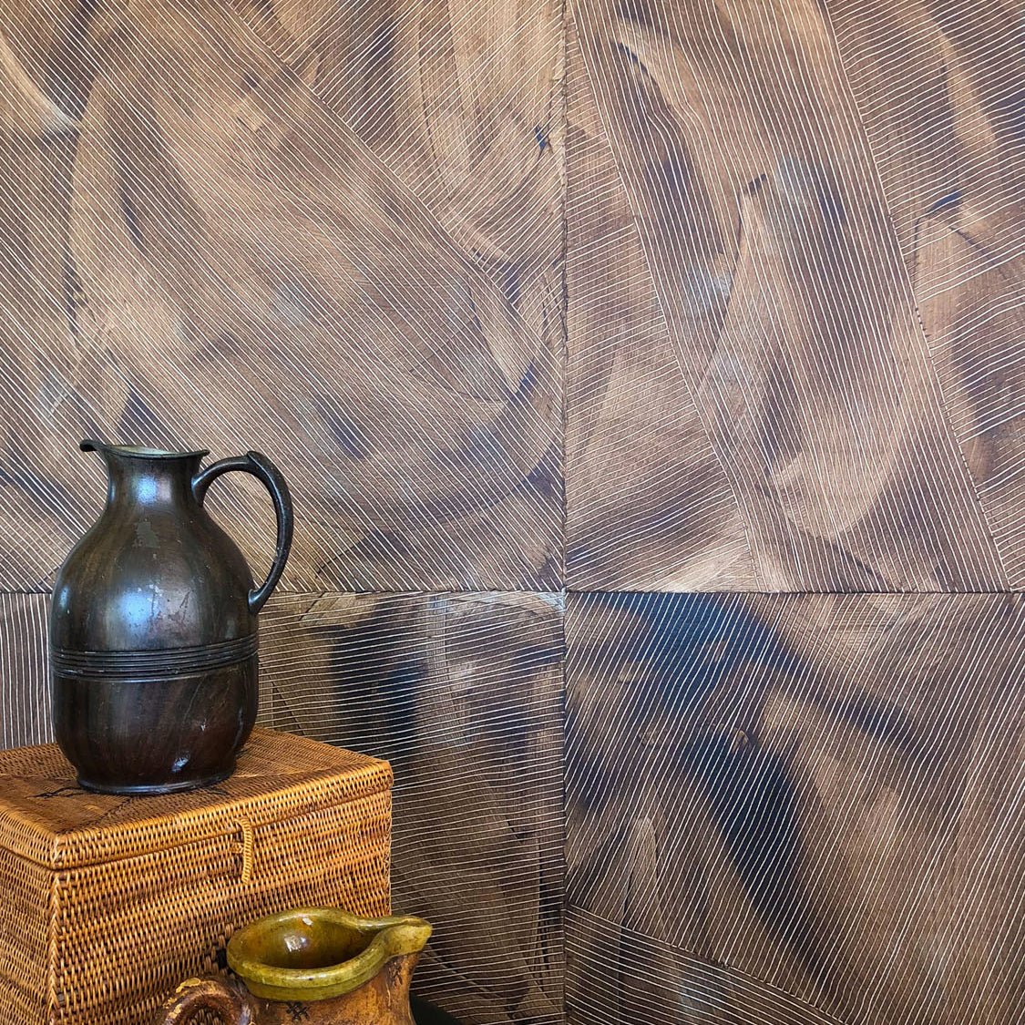 Vases stacked in front of a wall covered in multi-directional combed wallpaper in mottled brown.