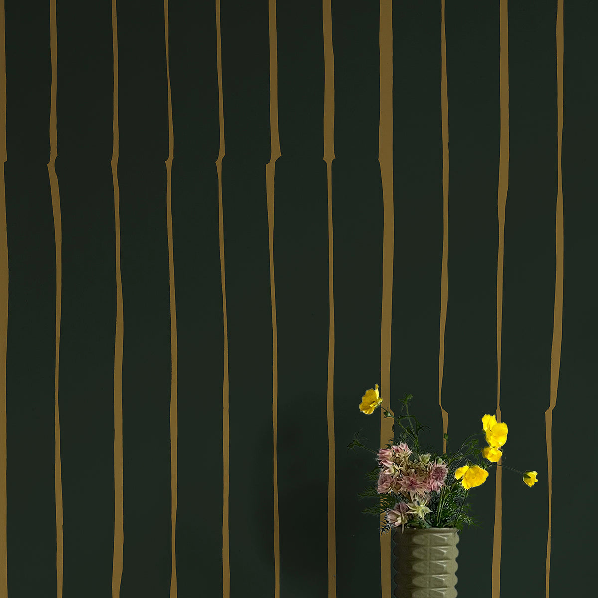 A vase of flowers stands in front of a wall covered in a playful irregular stripe print in mustard on a black field.