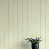 A vase of flowers stands in front of a wall covered in a playful irregular stripe print in light green on a cream field.