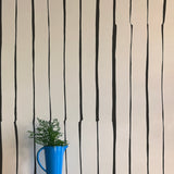 A vase of flowers stands in front of a wall covered in a playful irregular stripe print in black on a cream field.