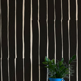 A vase of flowers stands in front of a wall covered in a playful irregular stripe print in cream on a black field.