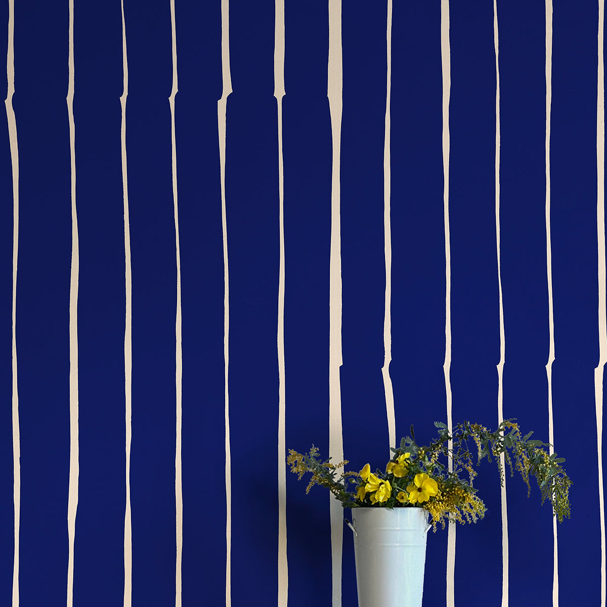 A vase of flowers stands in front of a wall covered in a playful irregular stripe print in cream on a navy field.