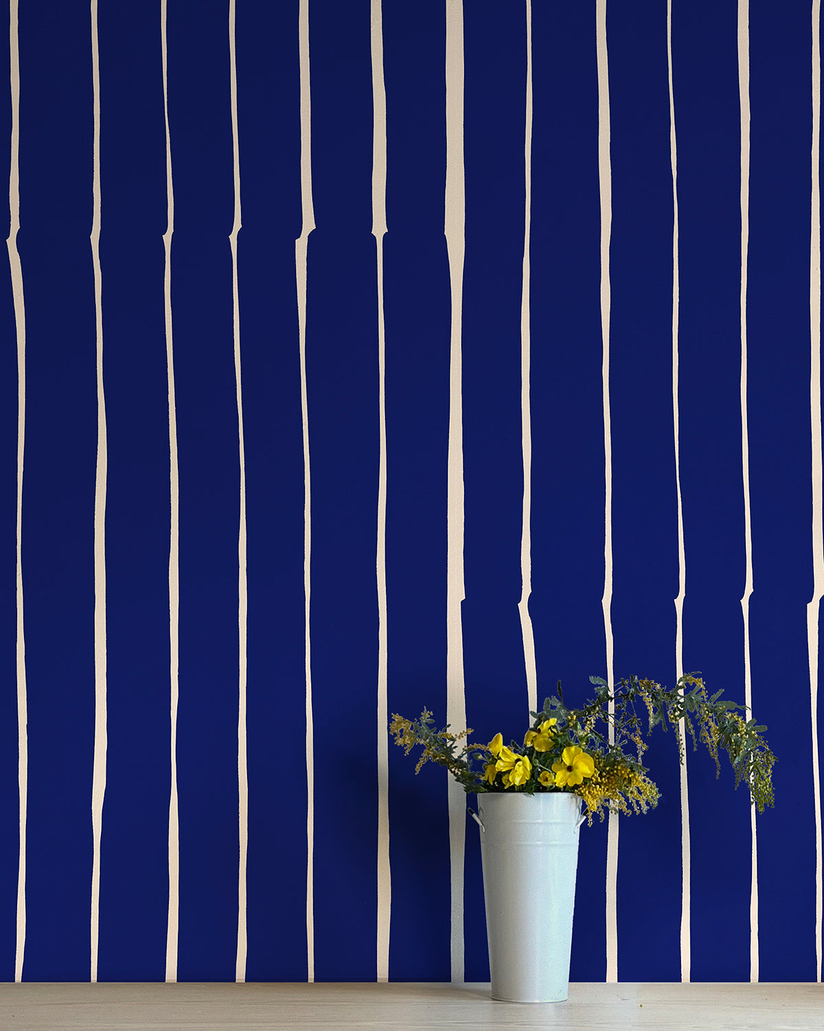 A vase of flowers stands in front of a wall covered in a playful irregular stripe print in cream on a navy field.