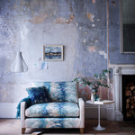 A chabby-chic living space with an armchair upholstered in an abstract paint blot pattern in green, blue and cream.