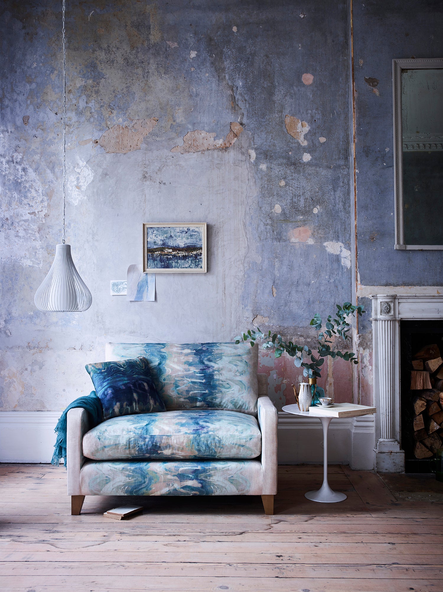 A chabby-chic living space with an armchair upholstered in an abstract paint blot pattern in green, blue and cream.