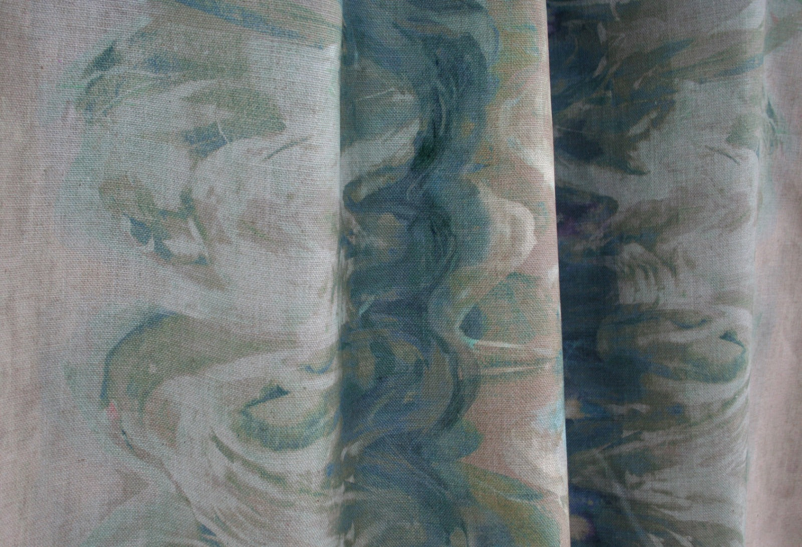 Close-up of draped fabric in an abstract paint blot pattern in shades of green, blue and cream.