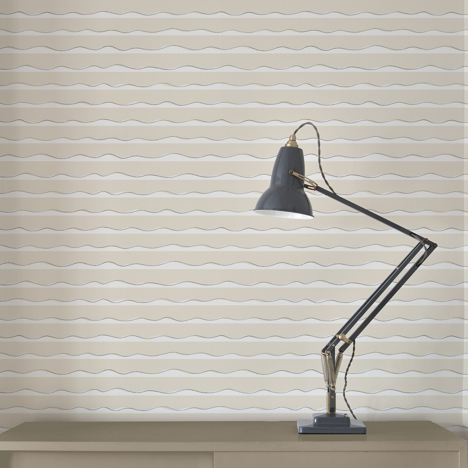A lamp stands in front of a wall papered in an undulating stripe pattern in cream and tan with black accents.
