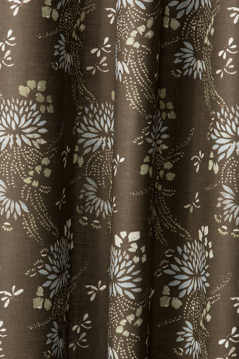 Draped printed fabric in a floral and dot pattern in beige and white on a brown field.