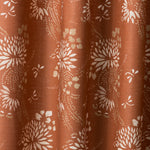 Draped printed fabric in a floral and dot pattern in white and gold on a rust field.