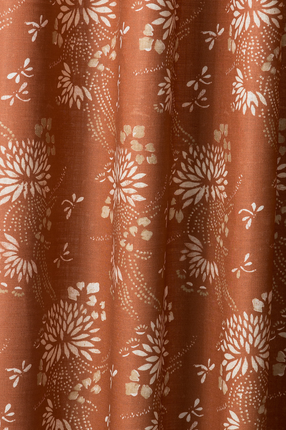 Draped printed fabric in a floral and dot pattern in white and gold on a rust field.