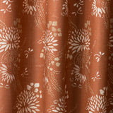 Draped printed fabric in a floral and dot pattern in white and gold on a rust field.